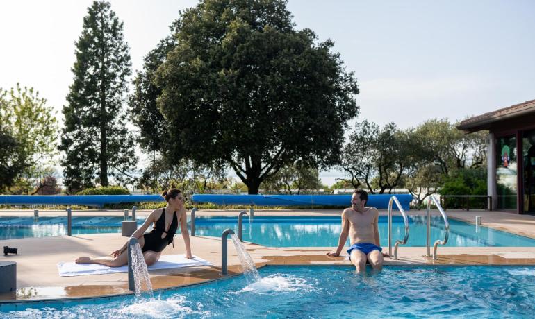 Zwei Personen entspannen am Pool mit Bäumen im Hintergrund.