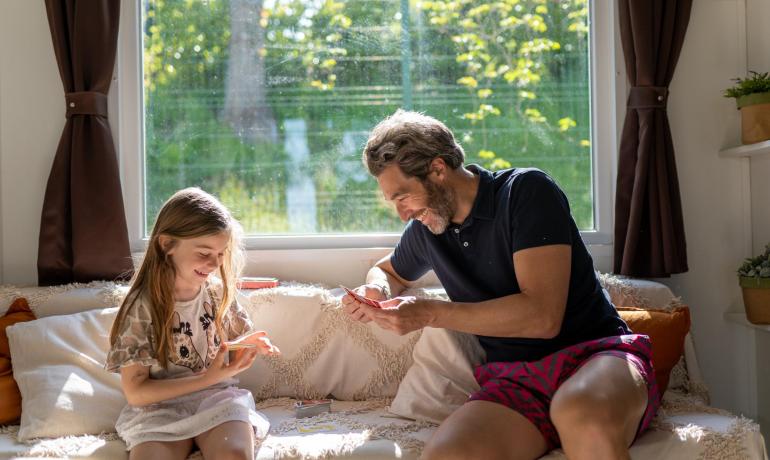 Vater und Tochter spielen Karten auf dem Sofa am Fenster.