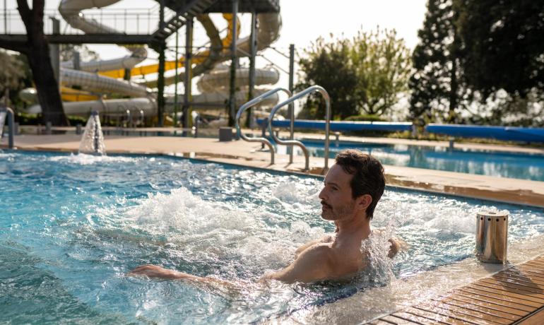 Uomo rilassato in piscina con scivoli sullo sfondo.