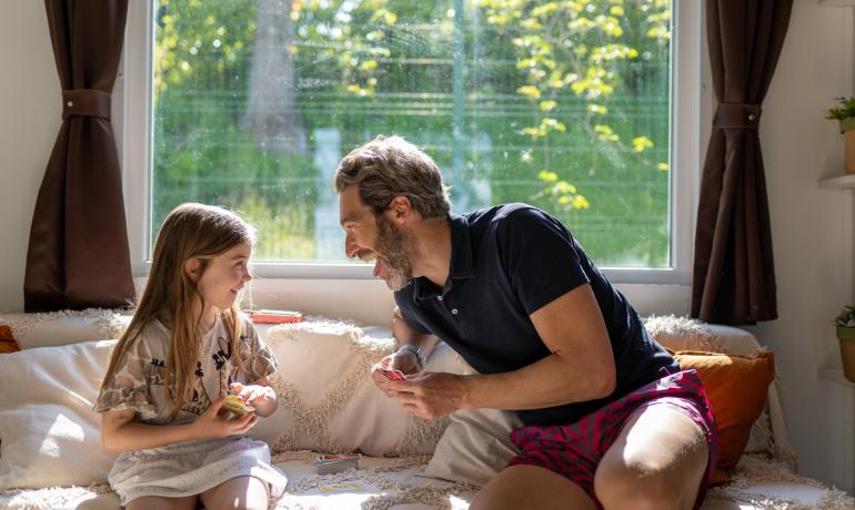 Vater und Tochter spielen Karten auf dem Sofa, lächelnd.