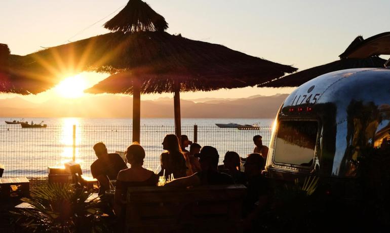 Beach sunset with people and straw umbrellas.